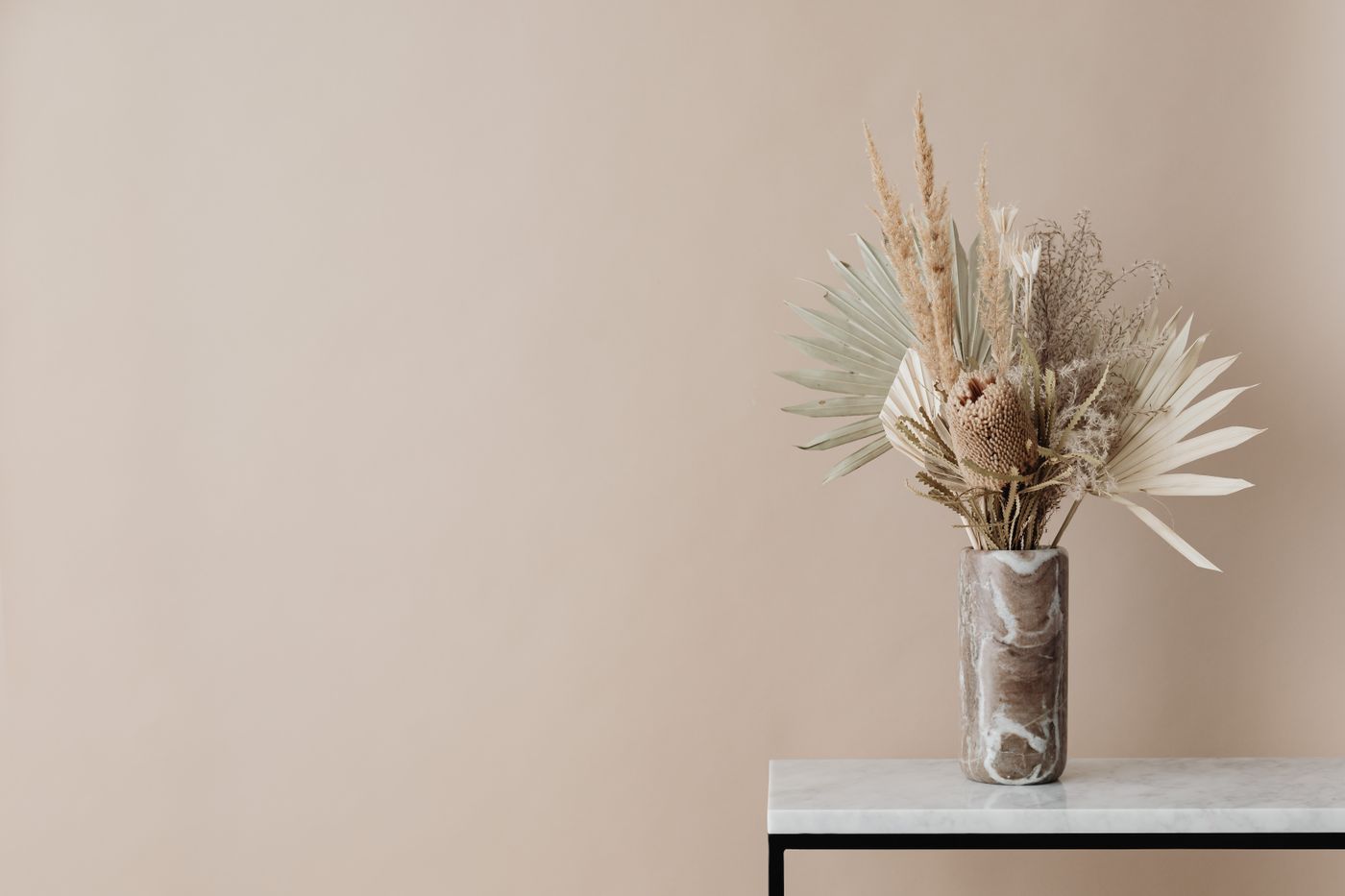 Dried botanicals in a marble vase on a table against a blush wall