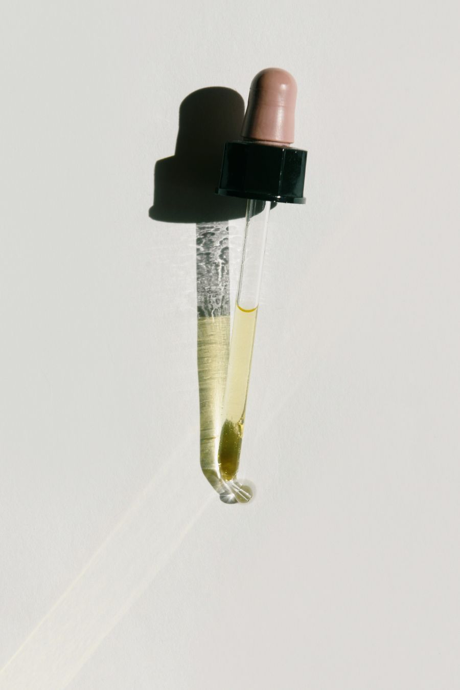 Glass dropper with golden oil in soft light against a warm white wall